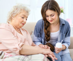 young woman rubbing an ointment to a senior woman's hand