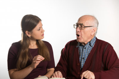 young woman helping senior man to pronounce sound and read book